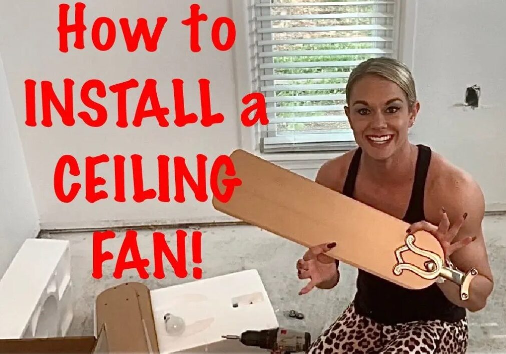 A woman holding up a cardboard fan with the words " how to install a ceiling fan !" on it.